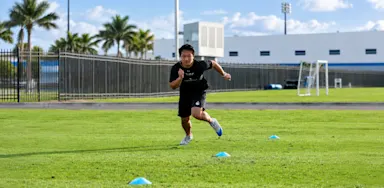 An athlete runs between cones on a grass field.