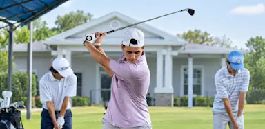 A golfer raises his club into a backswing while two other golfers practice nearby.