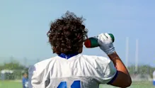 IMG Academy football player wearing jersey number 11 drinks from a water bottle during outdoor practice, highlighting hydration and recovery.