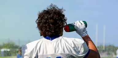IMG Academy football player wearing jersey number 11 drinks from a water bottle during outdoor practice, highlighting hydration and recovery.