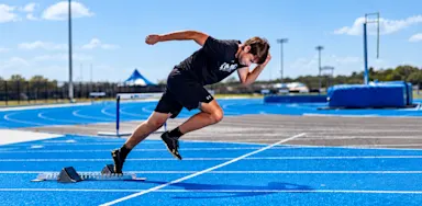 A sprinter accelerates out of starting blocks on a blue track.