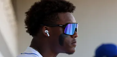 An athlete wearing sunglasses and earbuds looks to the side.