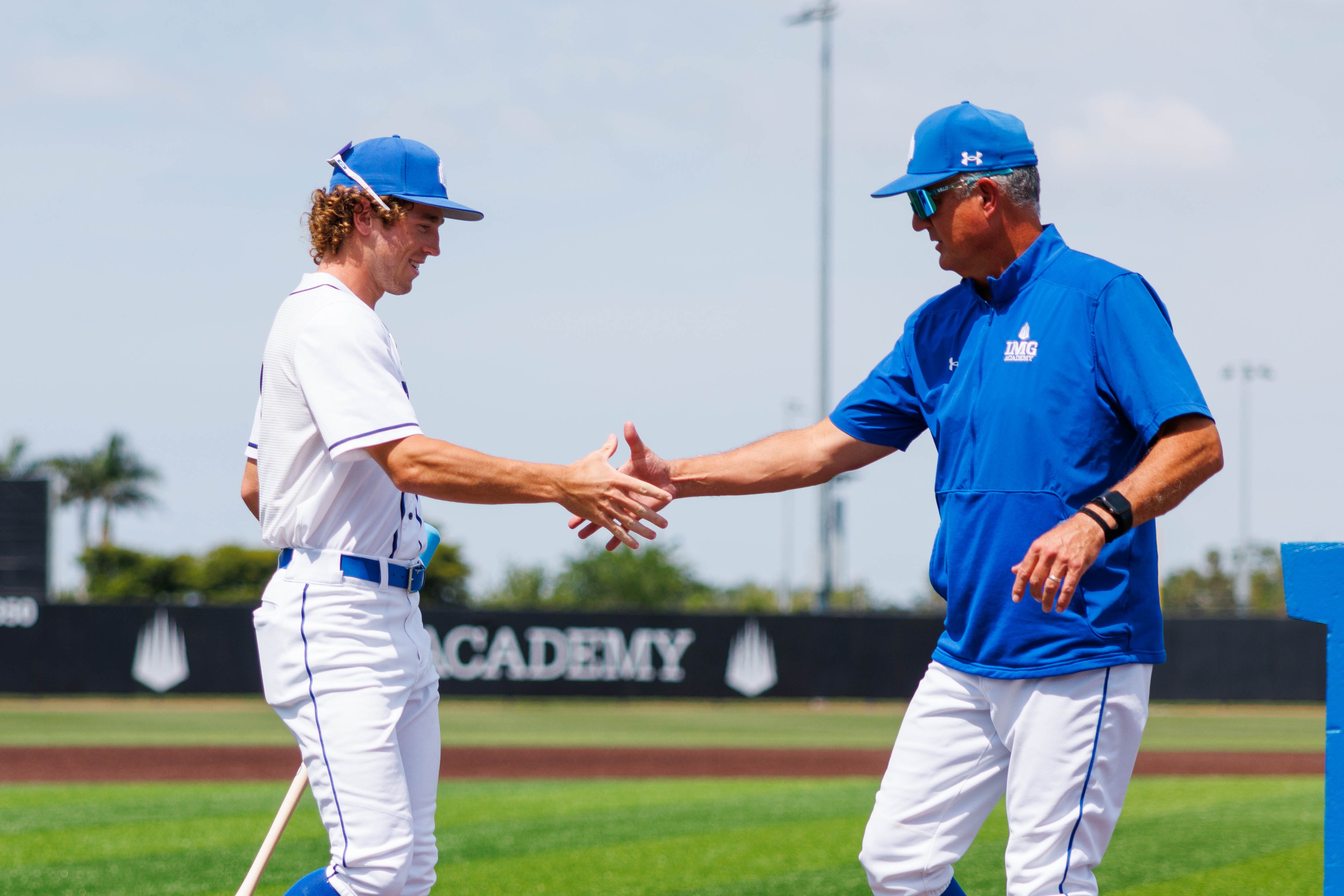 Baseball coach and student-athlete shaking hands on the field at IMG Academy, symbolizing the connection and communication central to the college recruiting process.