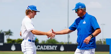 A baseball player shakes hands with a coach on the field.