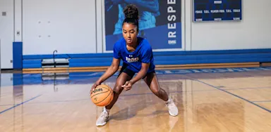 A basketball player crouches low while dribbling on an indoor court.