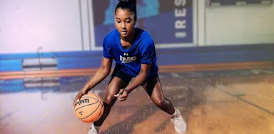 IMG Academy basketball athlete practices ball-handling drills on an indoor court, focused in an athletic stance during training.