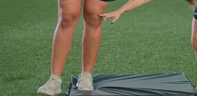 A trainer points to an athlete’s knee during a step-down exercise.
