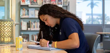 A student writes in a notebook at a table.