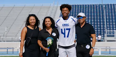 A football player poses with family members in a stadium.