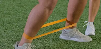 A close view shows an athlete stepping sideways with a resistance band around the ankles.