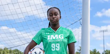 A soccer goalkeeper holds a ball while standing in front of a net.