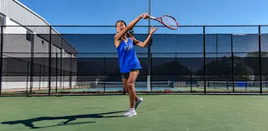 A tennis player swings a racket on an outdoor court.