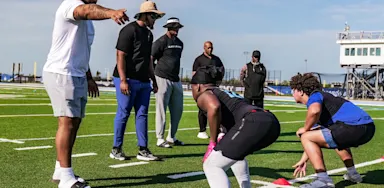 Football players performing drills under coach supervision during a recruiting evaluation, highlighting the importance of athletic performance in college recruitment.