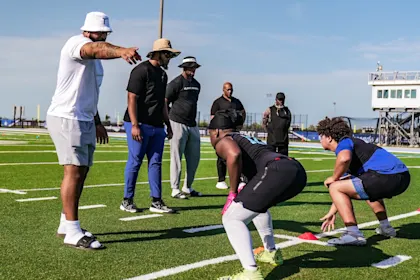 Football players performing drills under coach supervision during a recruiting evaluation, highlighting the importance of athletic performance in college recruitment.