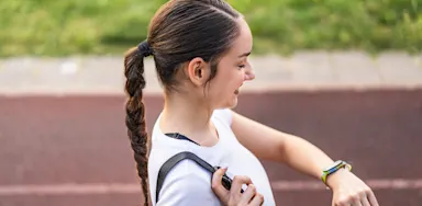 An athlete checks her watch beside a running track.