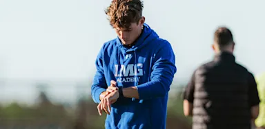 An athlete checks his watch while standing outdoors.