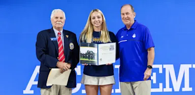 A student-athlete holds a certificate while posing with two adults.