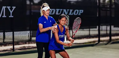 A tennis coach guides a player’s stance and racket position on a court.