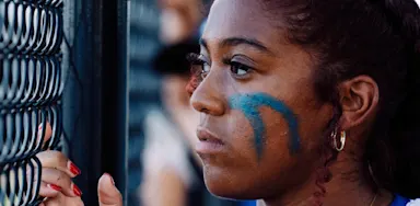 An athlete with face paint looks through a chain-link fence.