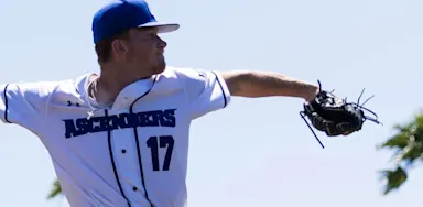 A baseball pitcher extends his gloved arm while preparing to throw.