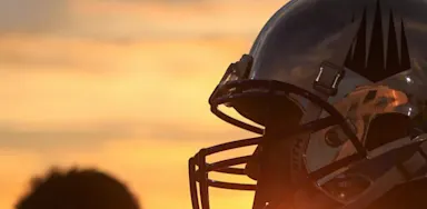 A close view shows a football helmet silhouetted against an orange sunset.