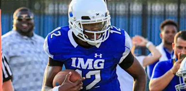 IMG Academy football player in a blue jersey running with the ball during a game, demonstrating focus and athletic performance.