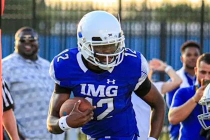 IMG Academy football player in a blue jersey running with the ball during a game, demonstrating focus and athletic performance.