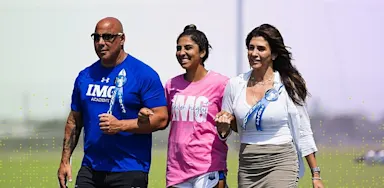 Student athlete walking arm-in-arm with two supportive adults on an IMG Academy campus, celebrating a milestone event.