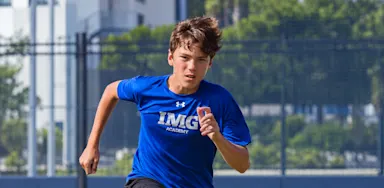 A student-athlete in a blue training shirt runs on an outdoor court.
