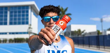 An athlete holds a sports-drink bottle toward the camera.