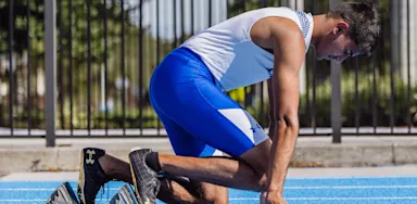 A sprinter kneels at starting blocks on a blue track.