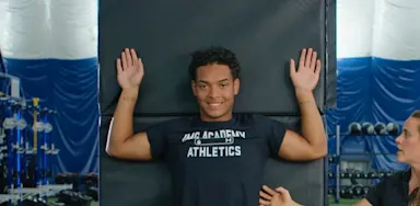An athlete holds both arms against a wall during a shoulder-mobility exercise.
