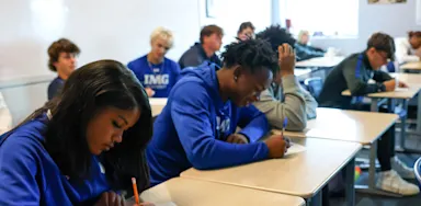 Students write at desks during a classroom lesson.
