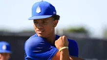 A baseball player in a blue uniform and cap performing a cross-body shoulder stretch during a recovery session.