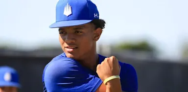 A baseball player in a blue uniform and cap performing a cross-body shoulder stretch during a recovery session.