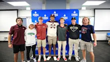 Group of IMG Academy student-athletes in college gear celebrating commitments to NCAA and NAIA programs, representing different collegiate athletic divisions.
