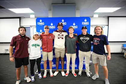 Group of IMG Academy student-athletes in college gear celebrating commitments to NCAA and NAIA programs, representing different collegiate athletic divisions.