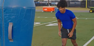 A football player prepares for a drill beside a padded training dummy.