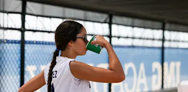 A tennis player drinks from a green bottle beside a court.