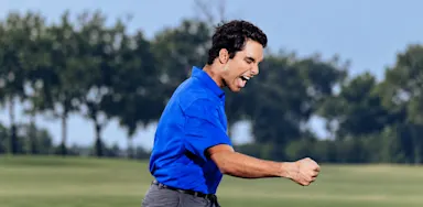 A golfer in a blue shirt celebrates on the course with a clenched fist.