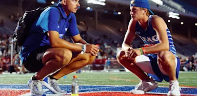 Track and Field coach and athlete reflecting while crouching on a track under stadium lights during Outdoor Nationals.