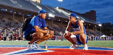 Two track athletes crouch together and talk beside a track.