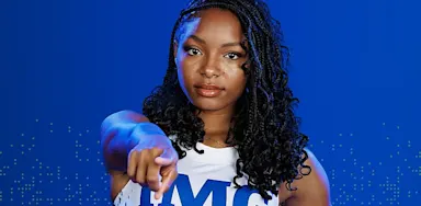 IMG Academy female student-athlete pointing forward against a blue background, conveying confidence, leadership, and personal accountability.