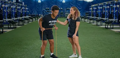 A trainer watches an athlete perform a resistance-band row.