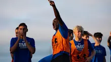 Boys Soccer athlete in IMG Academy gear cheering loudly and pointing skyward during a competitive practice session or game day huddle.