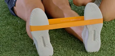 A close view shows a resistance band stretched around an athlete’s feet.