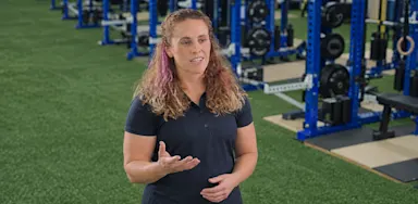 A trainer gestures while explaining an exercise in the weight room.