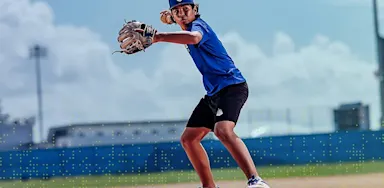 IMG Academy baseball athlete fields a ground ball on the infield during practice, wearing a blue uniform and glove, with focused posture and ready stance on a sunny day.