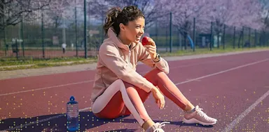 Young IMG Academy athlete sitting on an outdoor track and eating an apple after training, representing healthy fueling, recovery nutrition, and balanced athletic lifestyle.