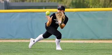 A softball player fields a ball while moving across the grass.